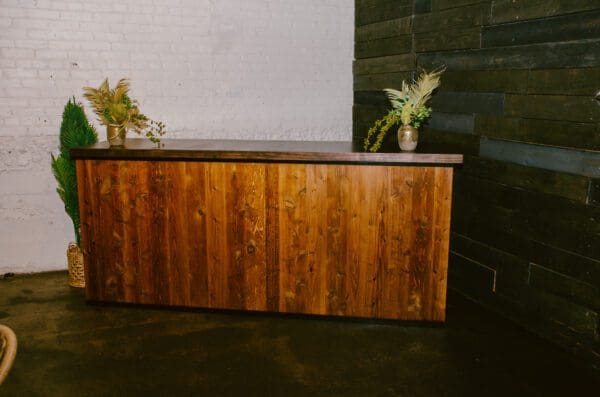 Sentence with product name: A Peak Wooden Bar with floral arrangements, against a white brick and dark wooden wall background.