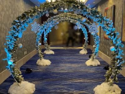 A festive event hallway decorated with a series of arches adorned with blue lights, snowflakes, and white winter accents.