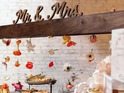 Decorative "mr. & mrs." sign above a wedding event buffet table adorned with suspended flowers.