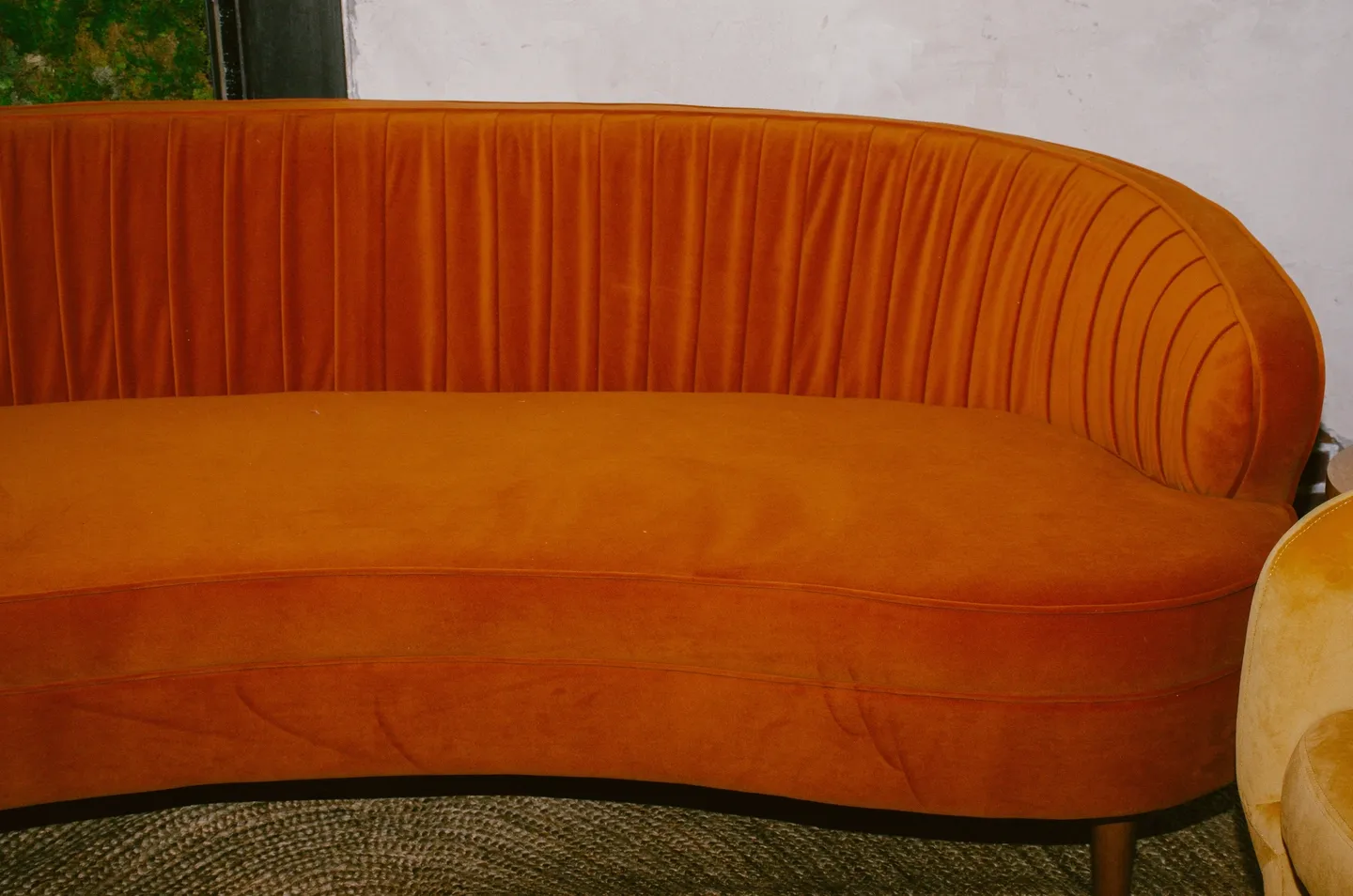 Orange upholstered curved sofa, ideal for events, with a pleated backrest.