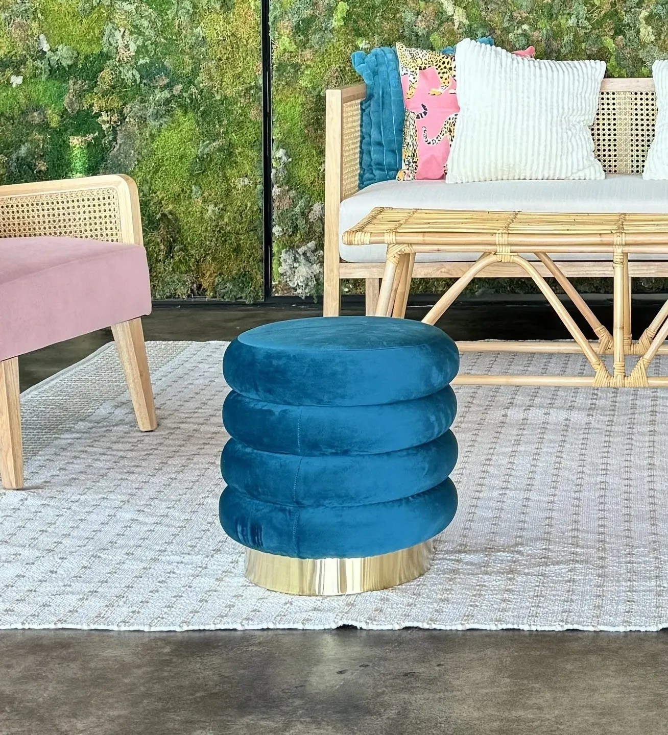 A plush blue ottoman with a gold base placed on a gray rug in a modern living room setting prepared for an event.