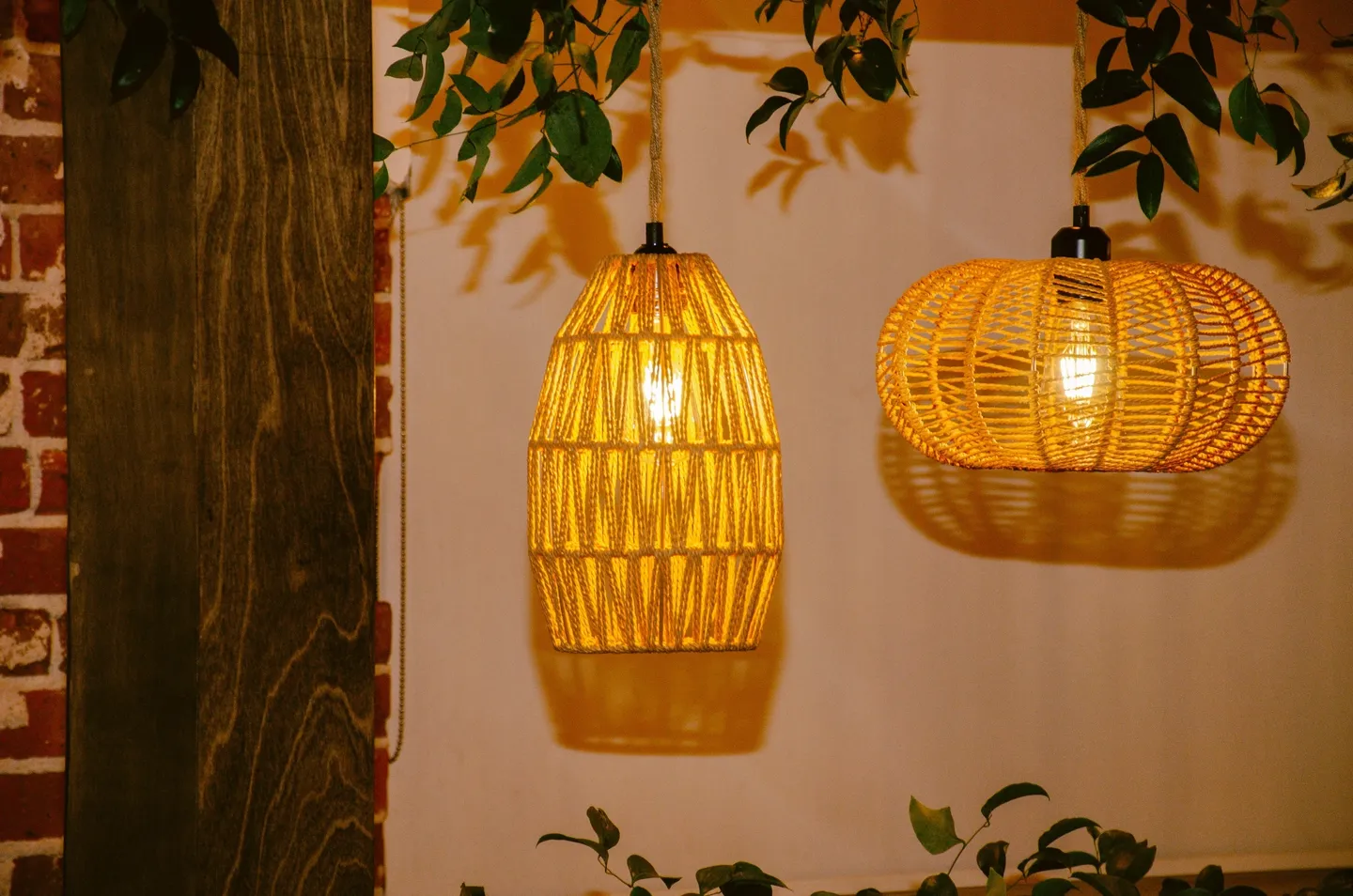 Two hanging wicker lamps casting warm light on a brick wall with plant decorations, setting an intimate ambiance for the event.
